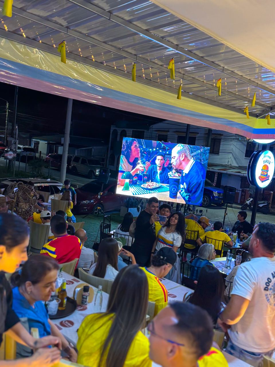 Pantalla LED en la terraza de un restaurante durante un montaje nocturno con público en las mesas
