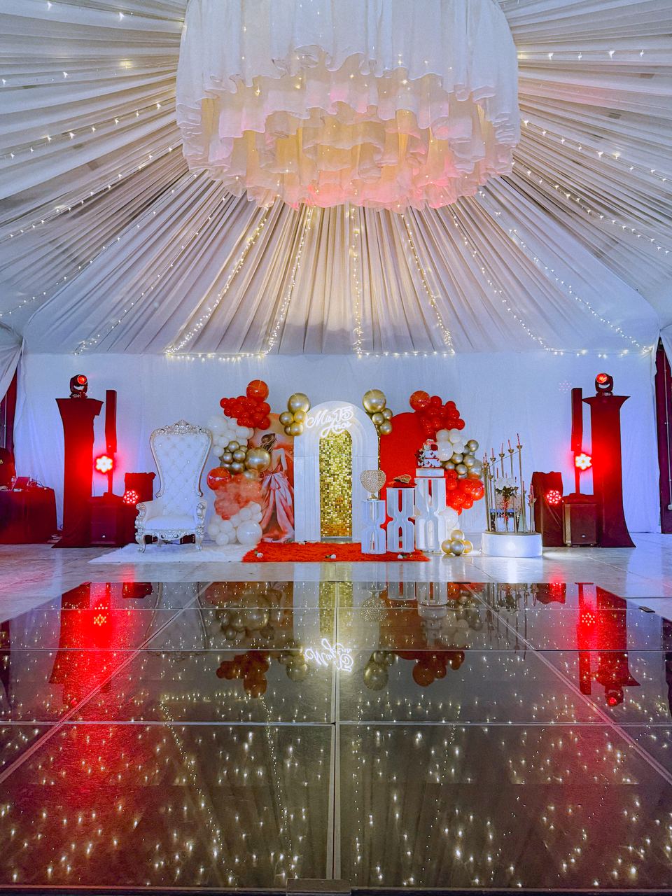 Montaje de quinceañera bajo carpa: pista de baile LED, luces robóticas, arco de globos y silla de trono
